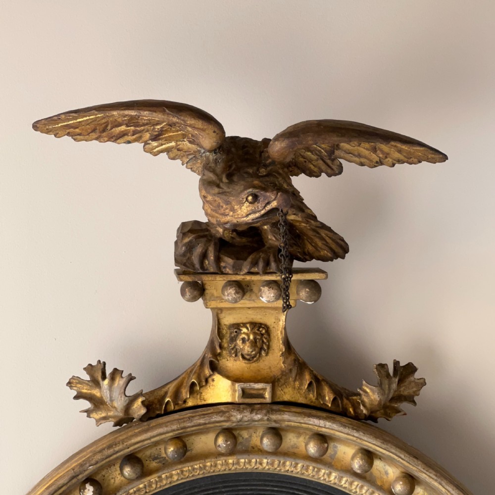 A circular Regency giltwood convex wall mirror topped with a carved eagle cresting and decorated with spherules along the frame. View VII