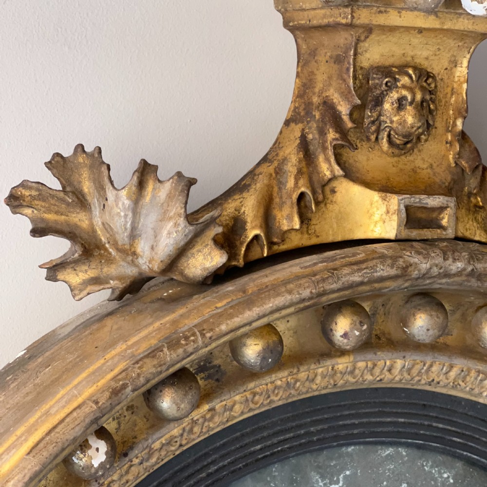 A circular Regency giltwood convex wall mirror topped with a carved eagle cresting and decorated with spherules along the frame. View VIII
