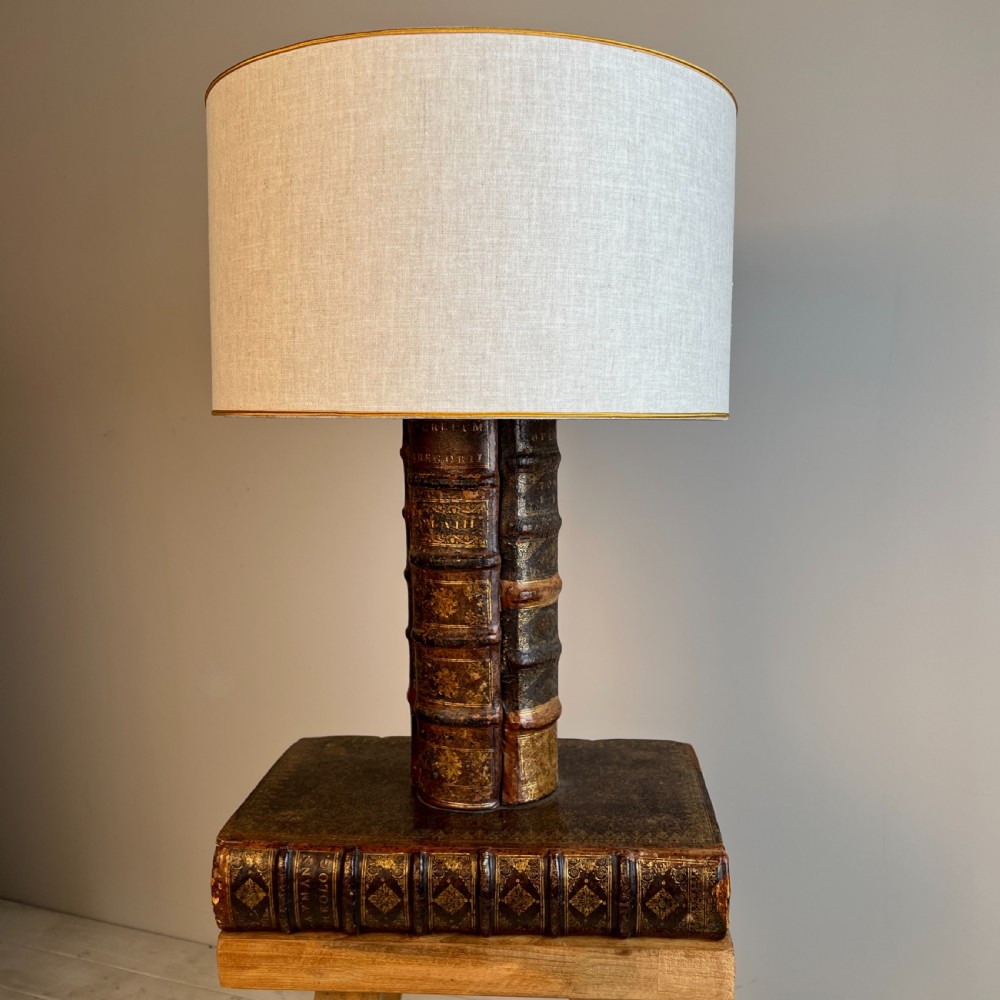 A table lamp featuring a column and base crafted from antique leather-bound book spines topped with a neutral drum shade. View II