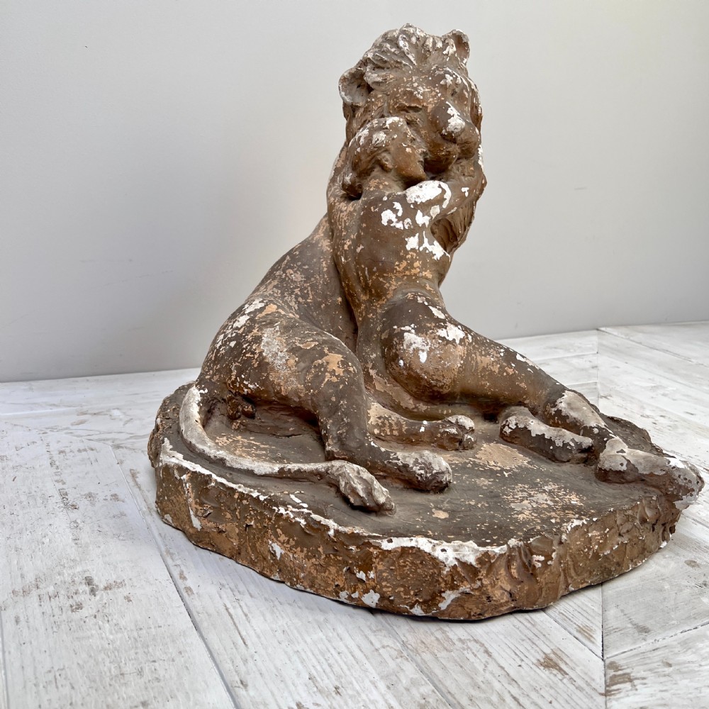 An antique brown terracotta and white painted plaster sculpture depicting a female figure embracing a lion on a naturalistic base.