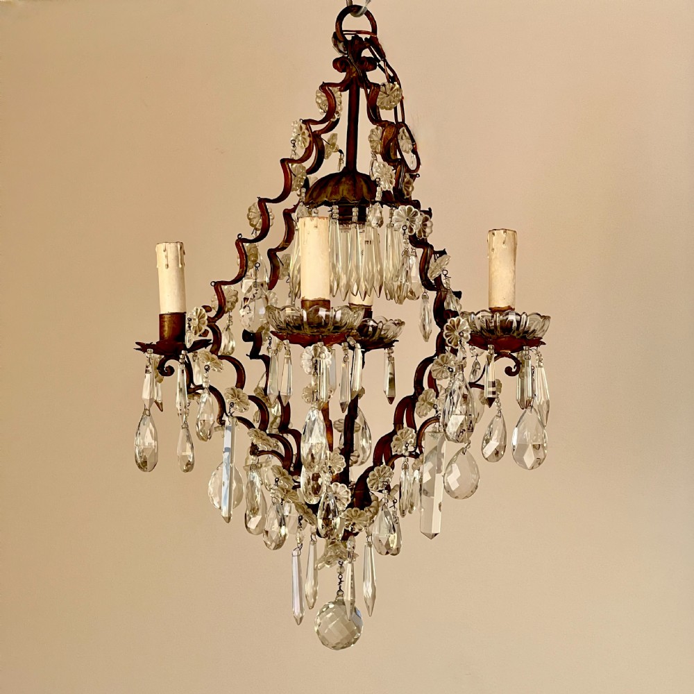 An antique French cage chandelier featuring an openwork metal frame decorated with clear glass rosettes, cut crystal teardrop prisms, and four candle-style light sockets.