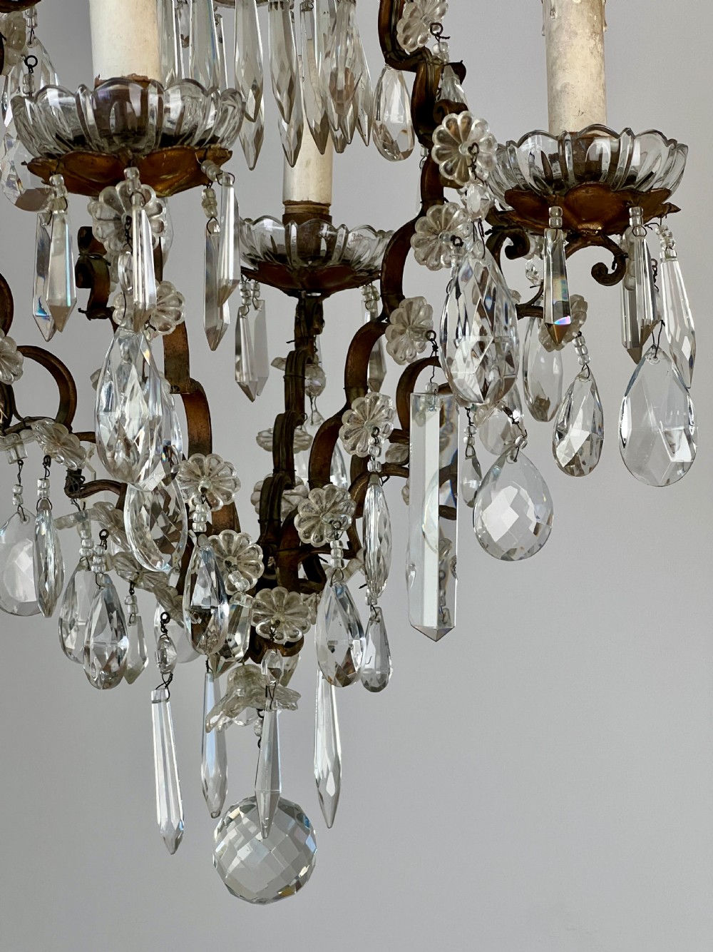 An antique French cage chandelier featuring an openwork metal frame decorated with clear glass rosettes, cut crystal teardrop prisms, and four candle-style light sockets. View III