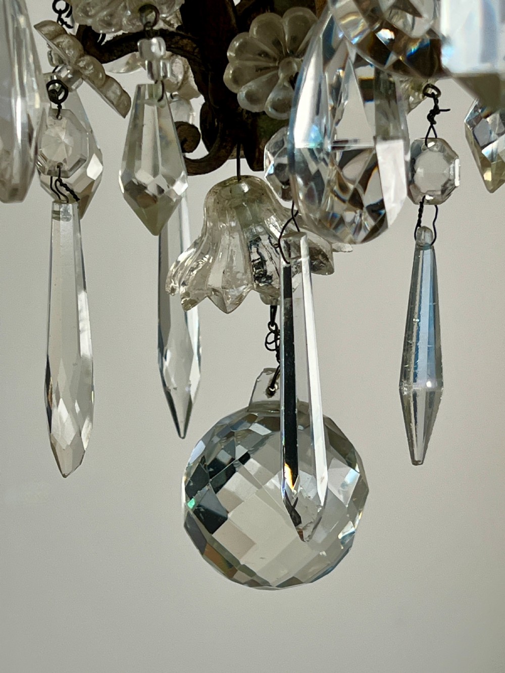 An antique French cage chandelier featuring an openwork metal frame decorated with clear glass rosettes, cut crystal teardrop prisms, and four candle-style light sockets. View V