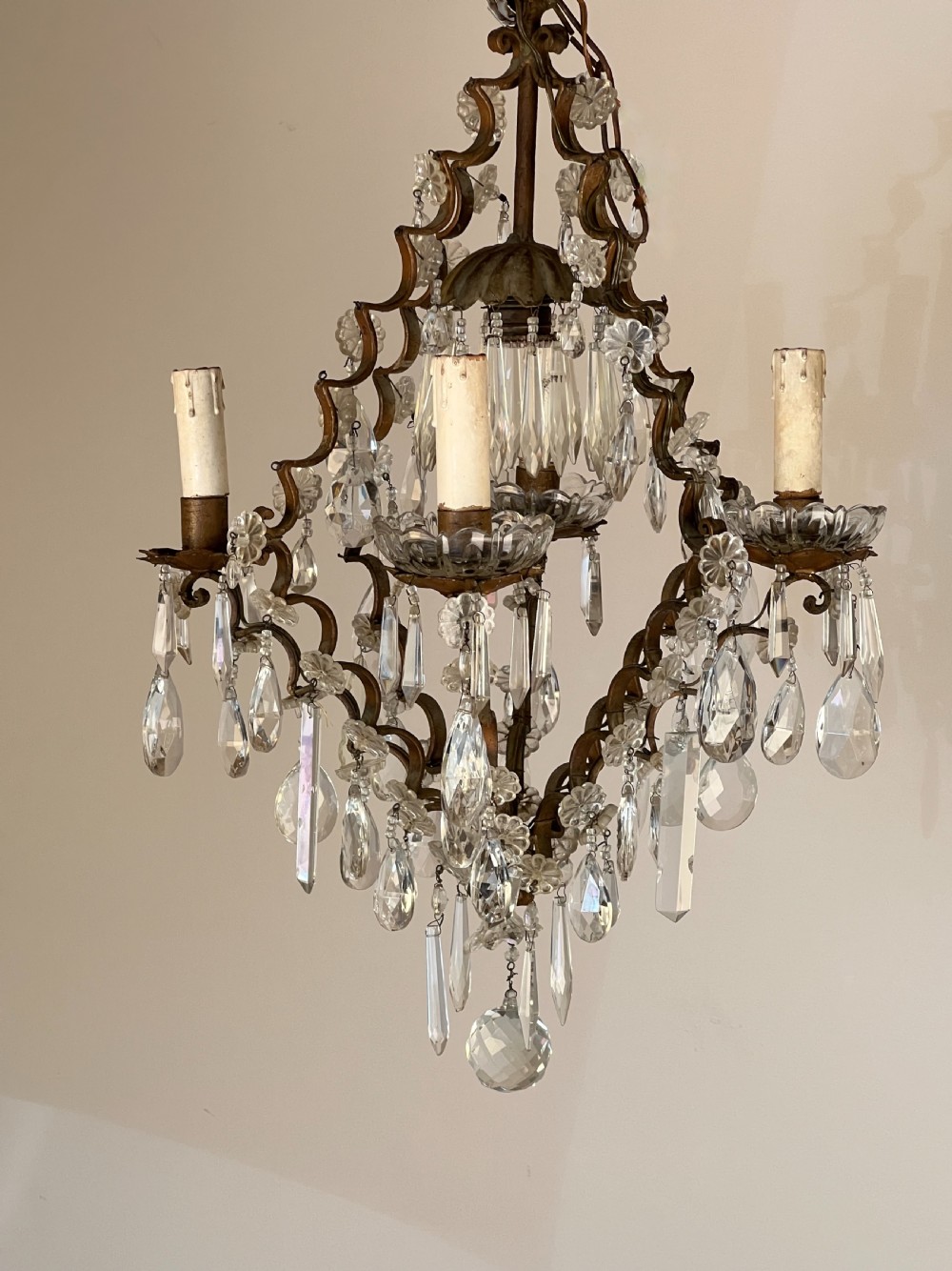 An antique French cage chandelier featuring an openwork metal frame decorated with clear glass rosettes, cut crystal teardrop prisms, and four candle-style light sockets. View VI