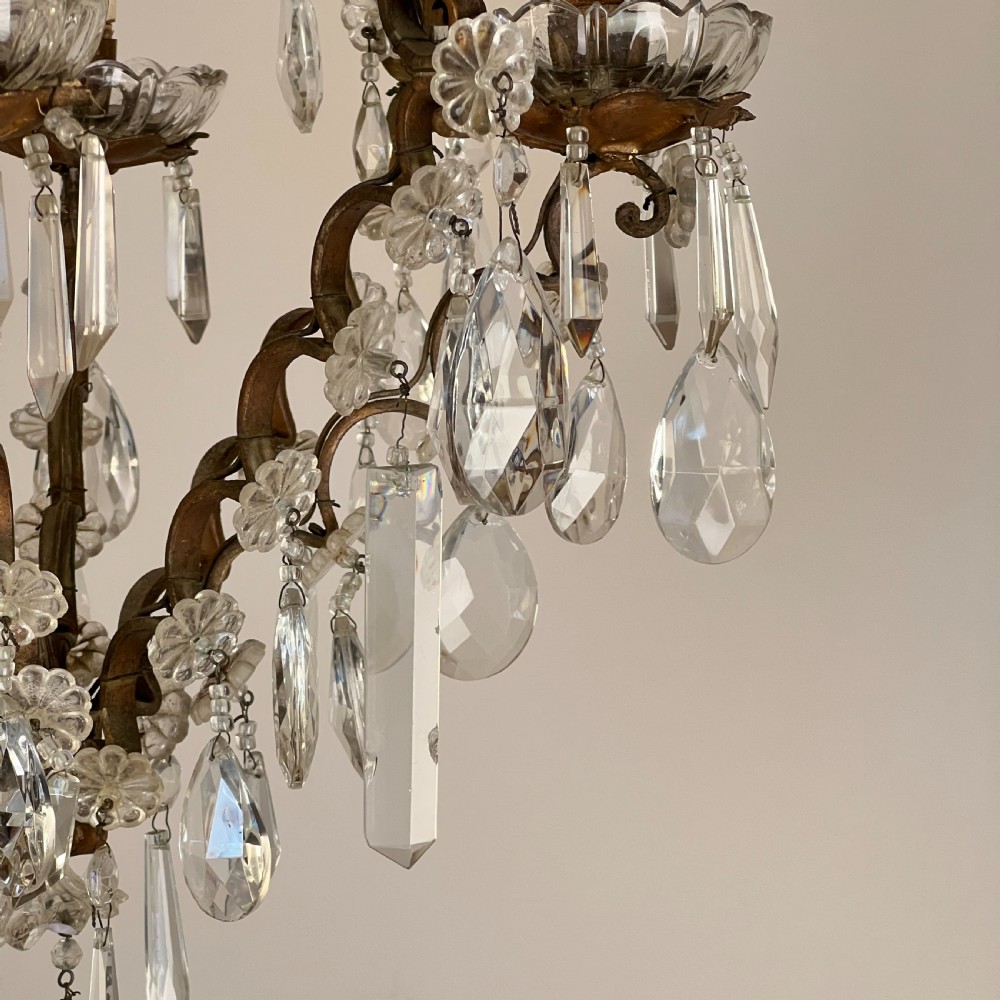 An antique French cage chandelier featuring an openwork metal frame decorated with clear glass rosettes, cut crystal teardrop prisms, and four candle-style light sockets. View VII