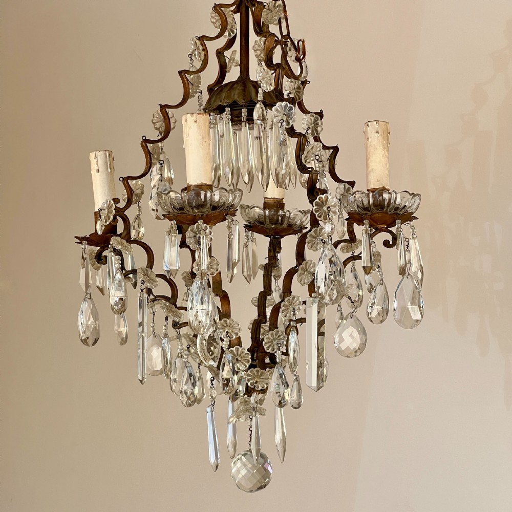 An antique French cage chandelier featuring an openwork metal frame decorated with clear glass rosettes, cut crystal teardrop prisms, and four candle-style light sockets. View VIII