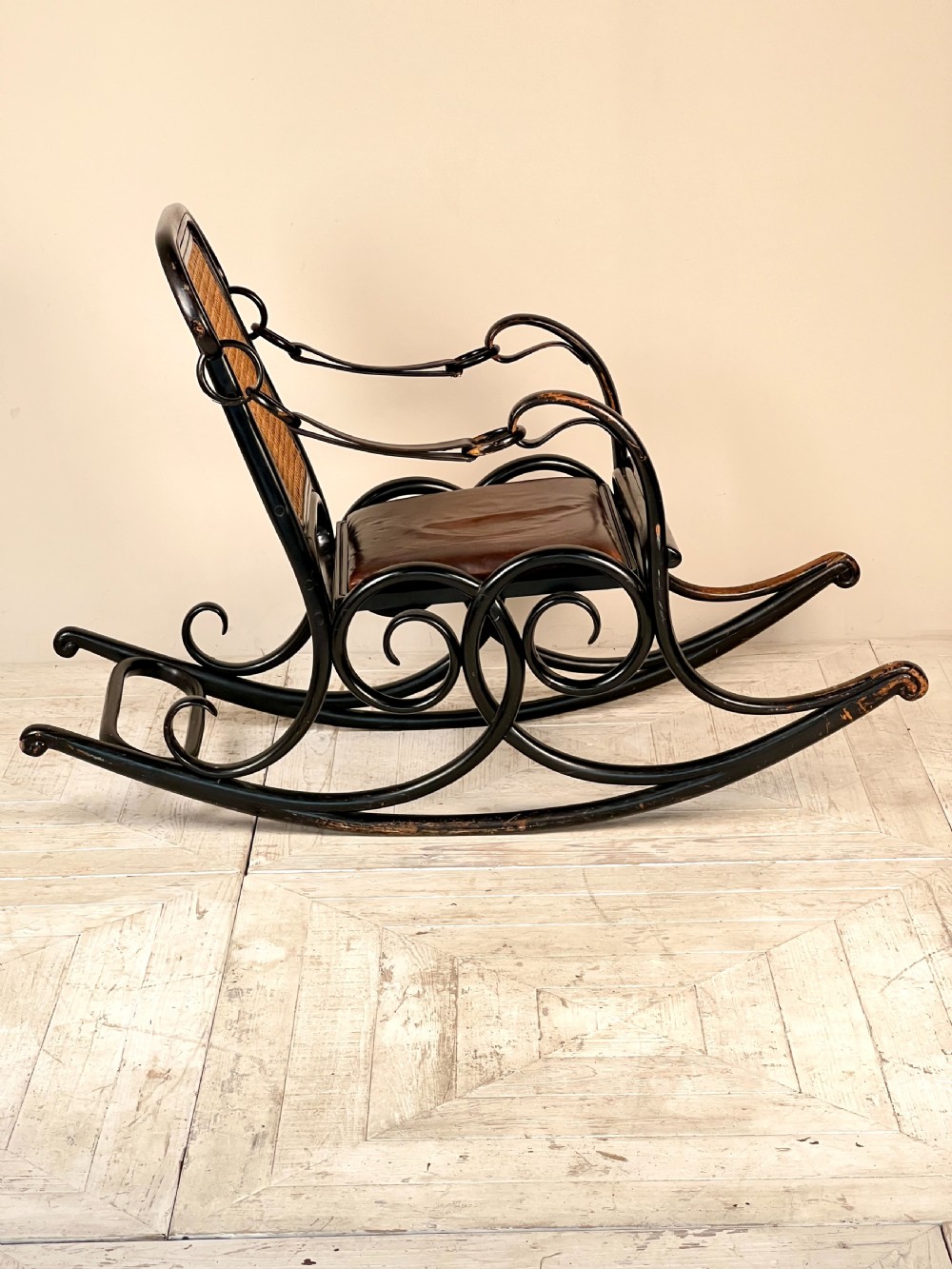 A dark brown steam-bent beechwood rocking chair featuring elaborate side scrollwork, a caned backrest, leather arm straps, and a dark leather padded seat. View VIII