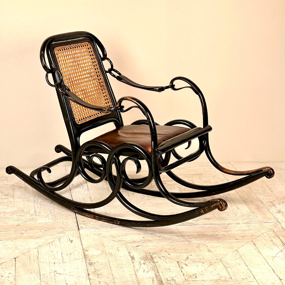 A dark brown steam-bent beechwood rocking chair featuring elaborate side scrollwork, a caned backrest, leather arm straps, and a dark leather padded seat. View IX