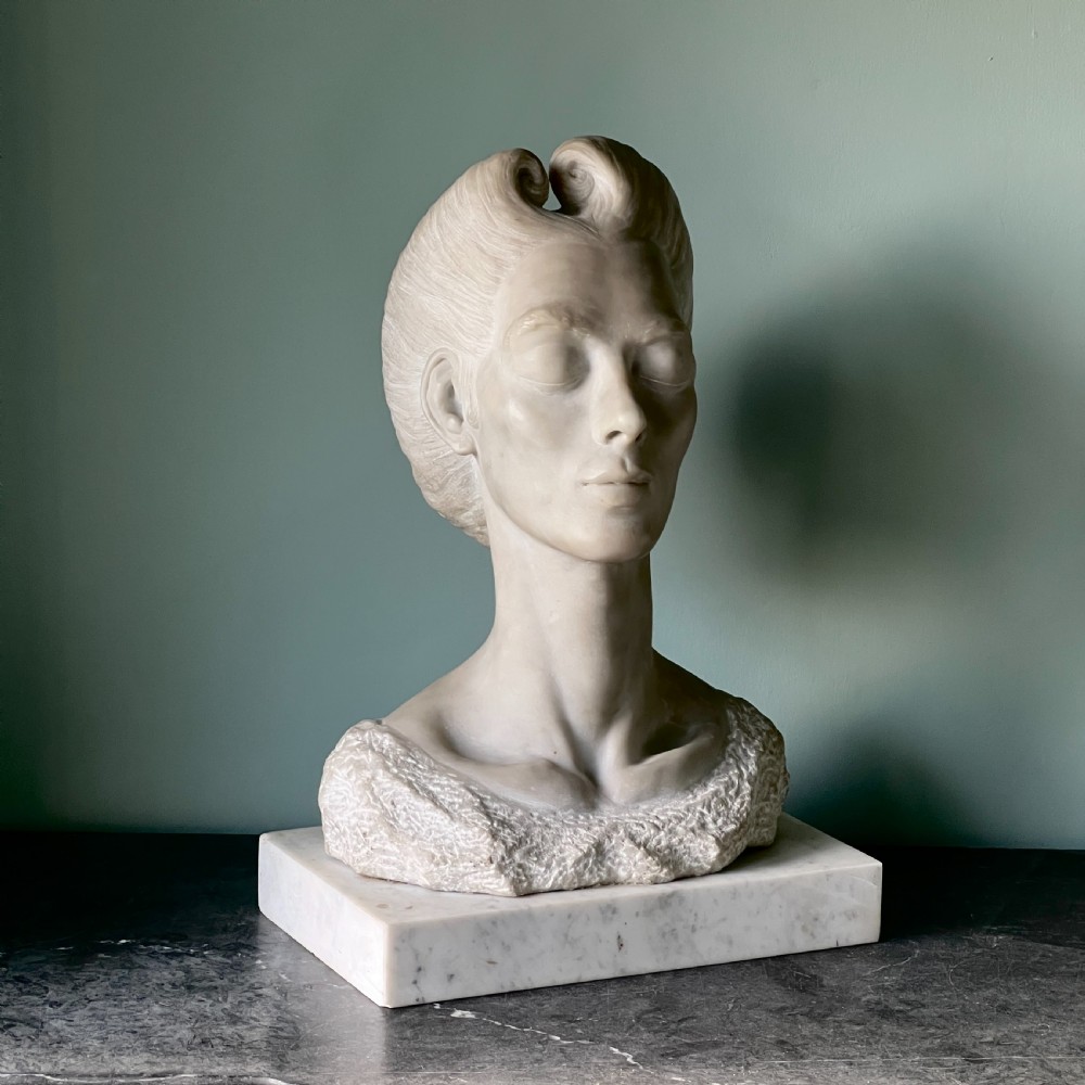 A carved off-white marble bust depicting a lady with styled hair and a serene expression, mounted on a matching square marble plinth.