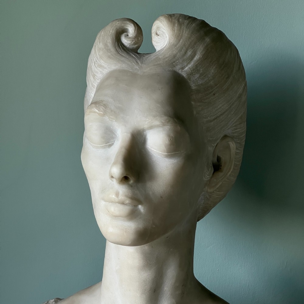 A carved off-white marble bust depicting a lady with styled hair and a serene expression, mounted on a matching square marble plinth. View II