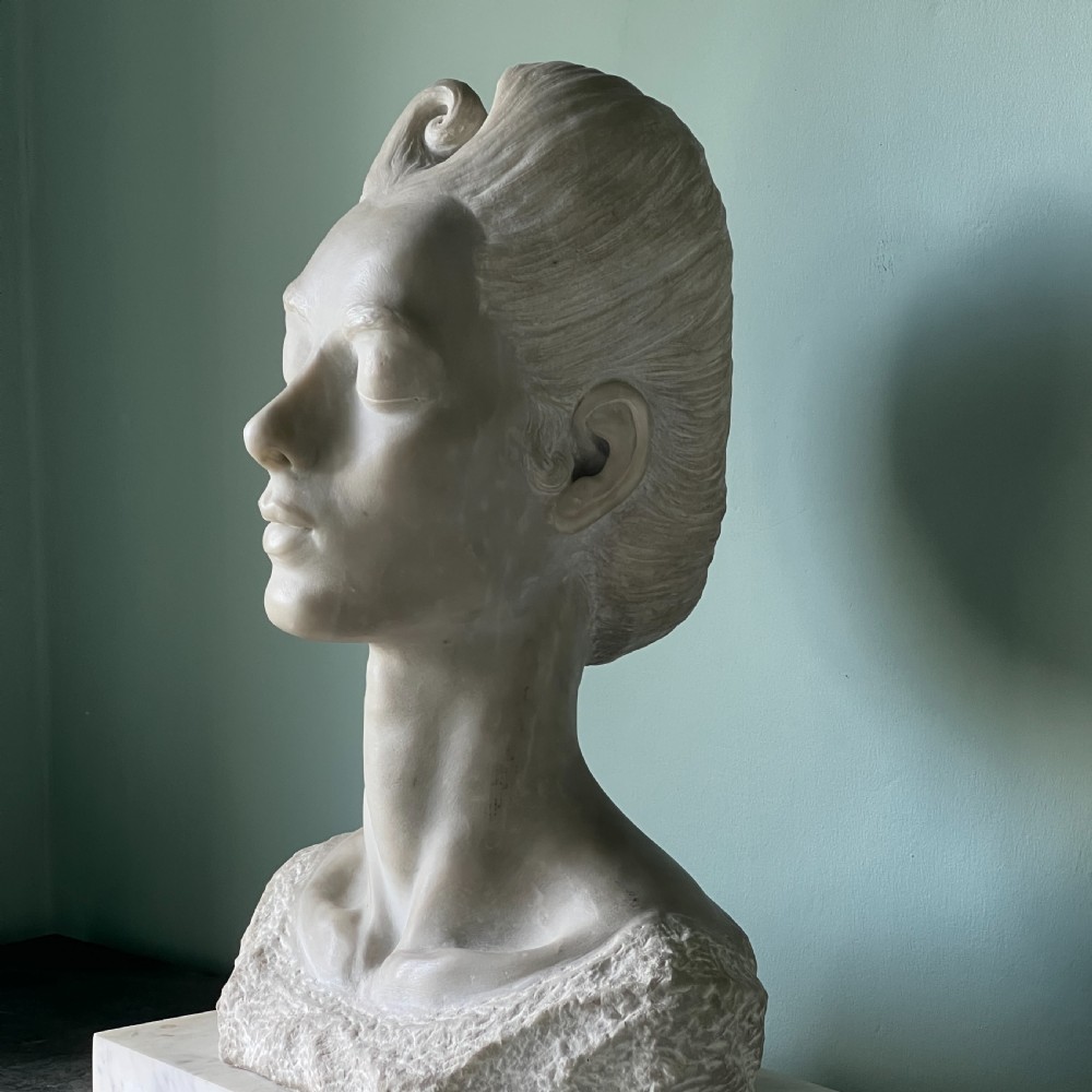 A carved off-white marble bust depicting a lady with styled hair and a serene expression, mounted on a matching square marble plinth. View III