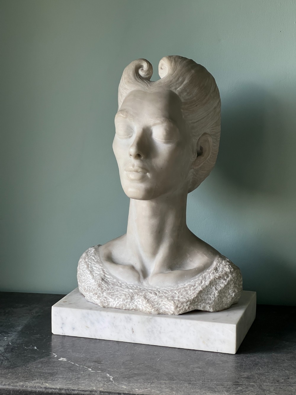 A carved off-white marble bust depicting a lady with styled hair and a serene expression, mounted on a matching square marble plinth. View IV
