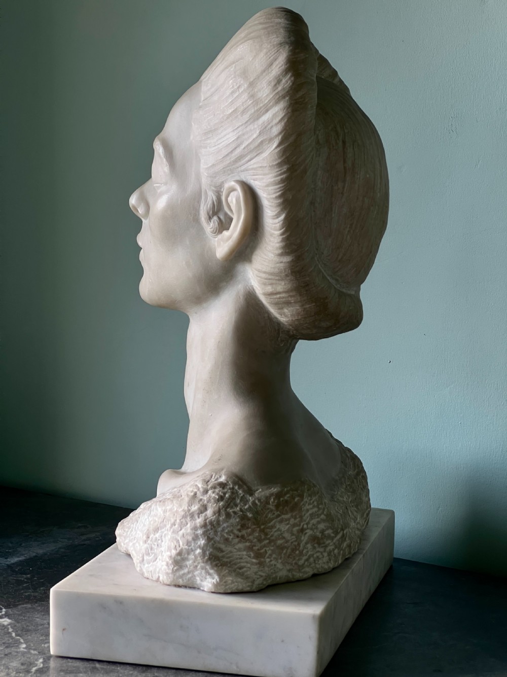 A carved off-white marble bust depicting a lady with styled hair and a serene expression, mounted on a matching square marble plinth. View V