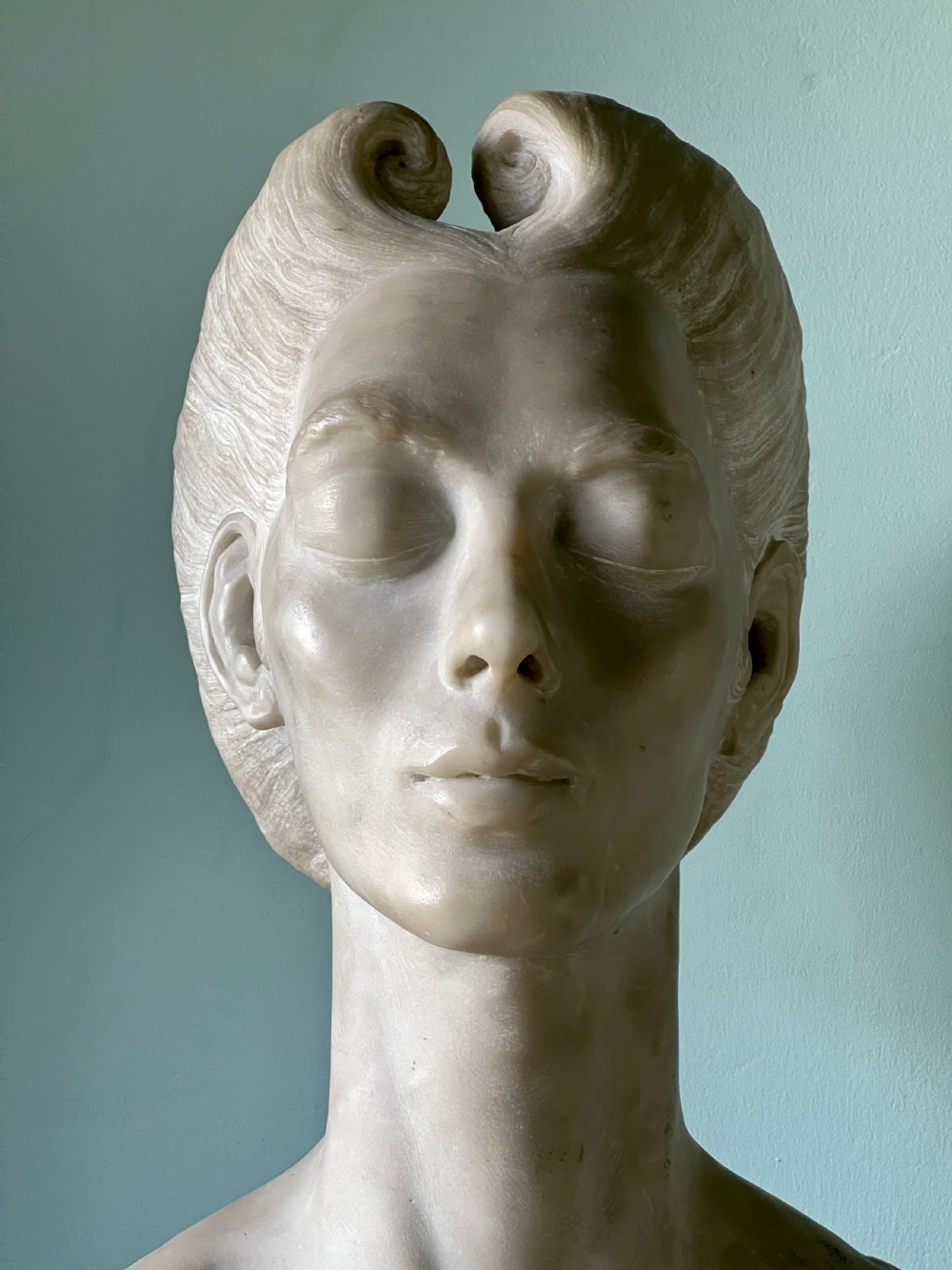 A carved off-white marble bust depicting a lady with styled hair and a serene expression, mounted on a matching square marble plinth. View VI