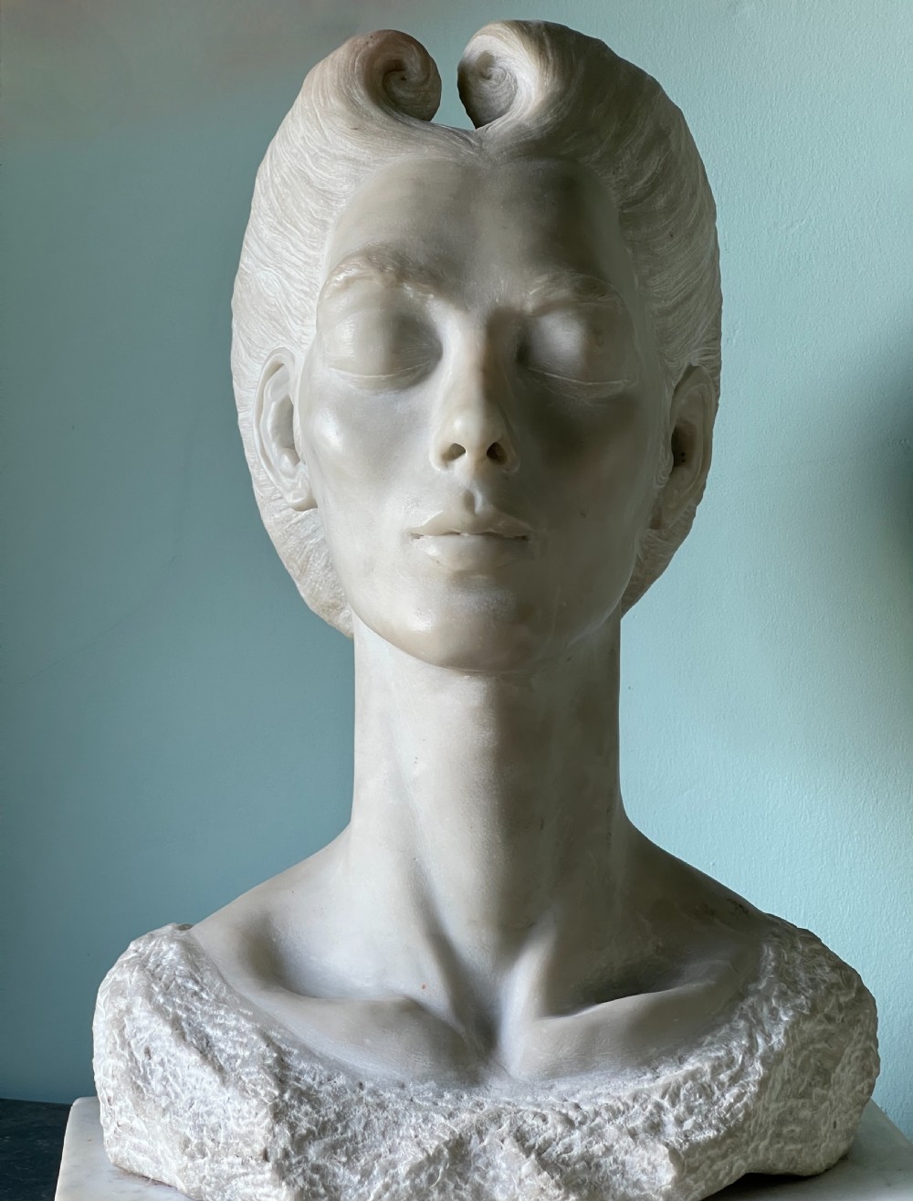 A carved off-white marble bust depicting a lady with styled hair and a serene expression, mounted on a matching square marble plinth. View VII