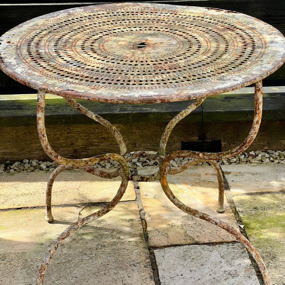 A circular French antique wrought iron garden table featuring a perforated metal top, curved legs with a central stretcher ring, and a heavily patinated weathered paint finish. View IV