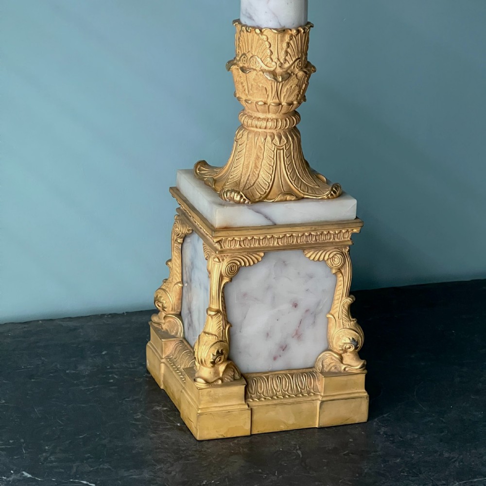 An Empire style table lamp featuring a white marble column base with gold ormolu leaf mounts and a large cream drum shade. View IV