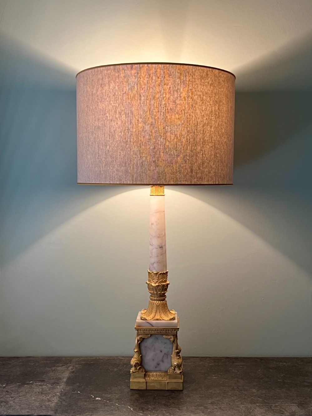 An Empire style table lamp featuring a white marble column base with gold ormolu leaf mounts and a large cream drum shade. View VI