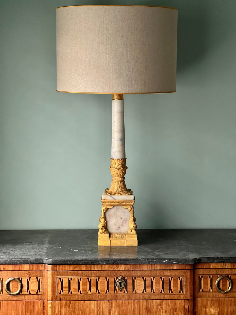 An Empire style table lamp featuring a white marble column base with gold ormolu leaf mounts and a large cream drum shade. View VIII
