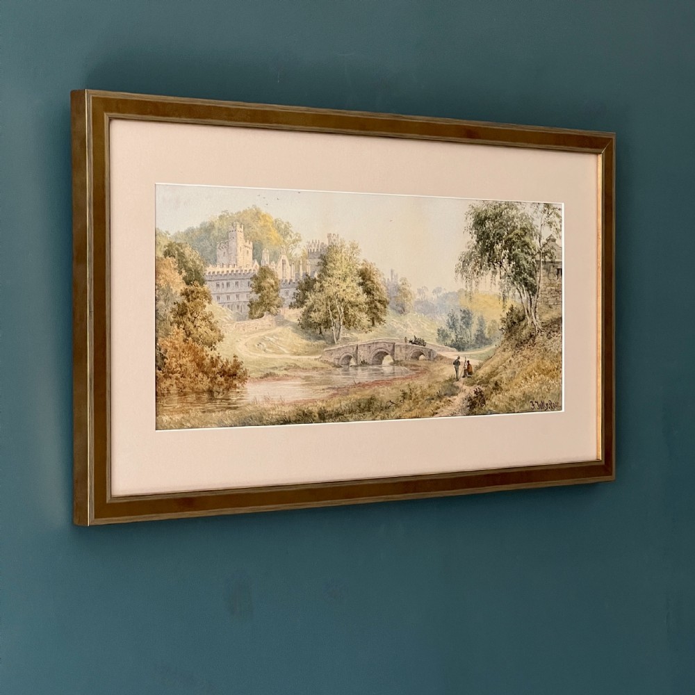 A framed Victorian watercolour painting depicting Windsor Castle beyond a river and stone bridge, framed in a gold-toned wooden frame with a cream mount.