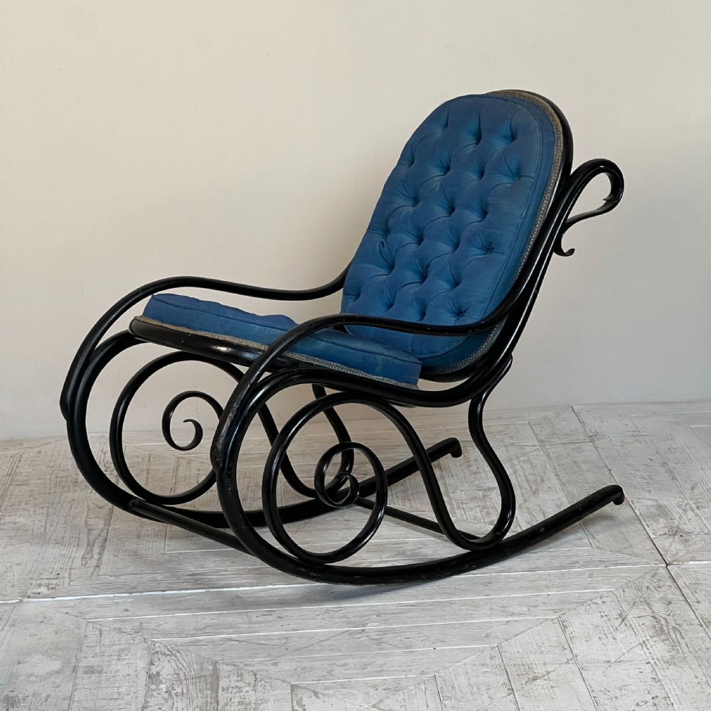 A Victorian ebonised bentwood rocking chair featuring elaborate curved scrollwork frame and deep blue button-tufted upholstery.