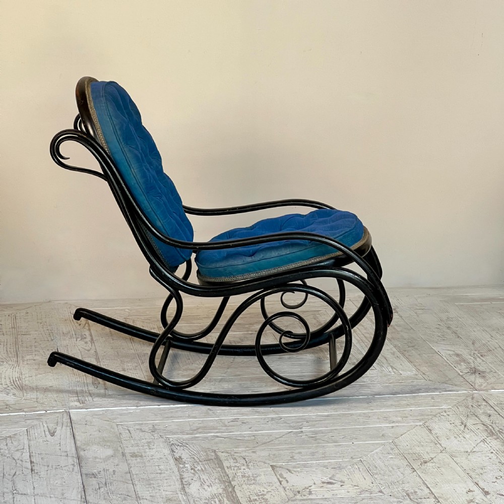 A Victorian ebonised bentwood rocking chair featuring elaborate curved scrollwork frame and deep blue button-tufted upholstery. View II