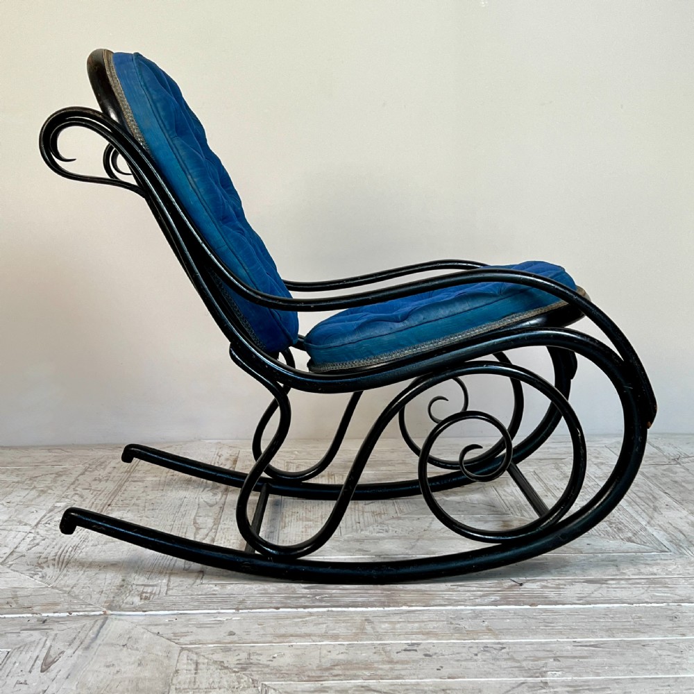 A Victorian ebonised bentwood rocking chair featuring elaborate curved scrollwork frame and deep blue button-tufted upholstery. View III
