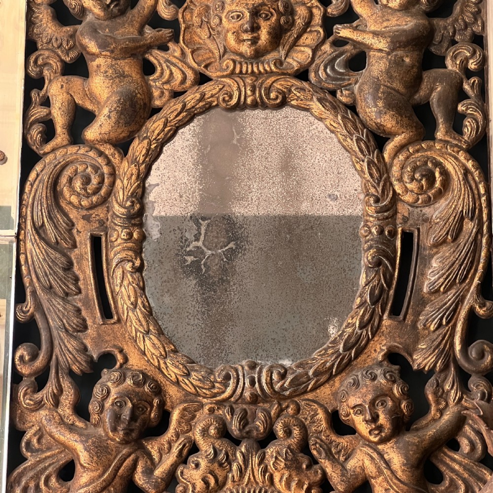 A rectangular gilded wall mirror featuring a central oval plate surrounded by relief carvings of putti and laurel leaves, flanked by two metal candle sconces. View VII