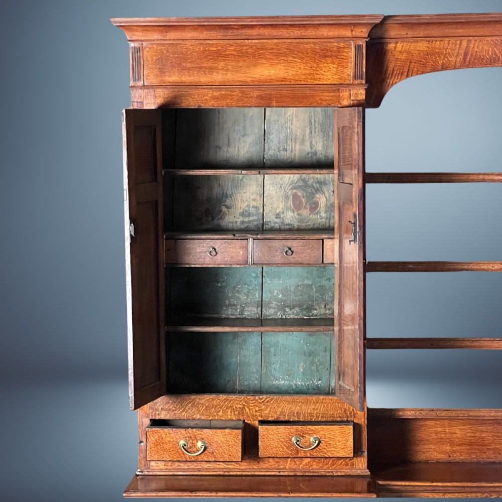 A large Georgian oak breakfront housekeepers cupboard featuring twin side cabinets with drawers, central open shelves, and brass swan-neck handles. View V