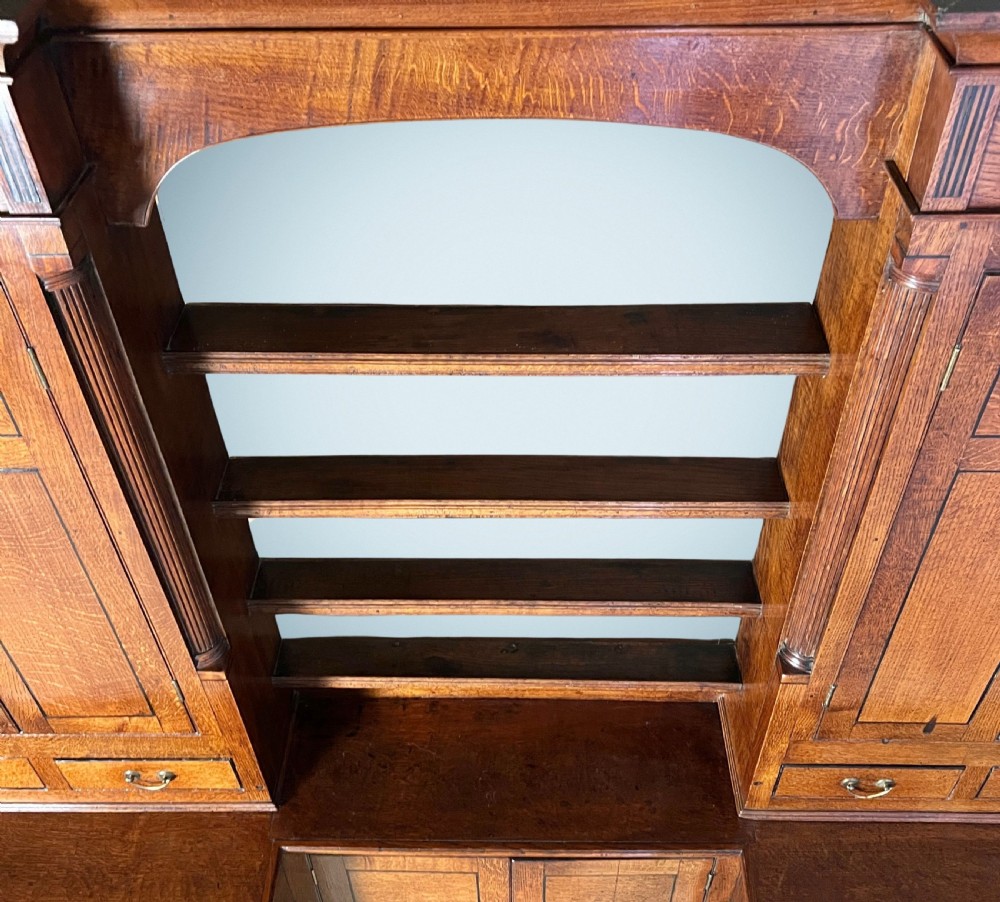 A large Georgian oak breakfront housekeepers cupboard featuring twin side cabinets with drawers, central open shelves, and brass swan-neck handles. View VII