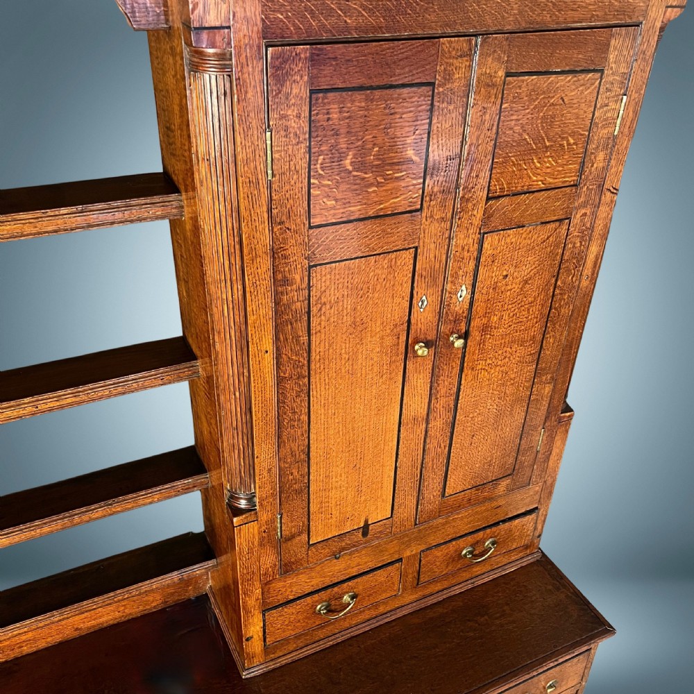 A large Georgian oak breakfront housekeepers cupboard featuring twin side cabinets with drawers, central open shelves, and brass swan-neck handles. View VIII