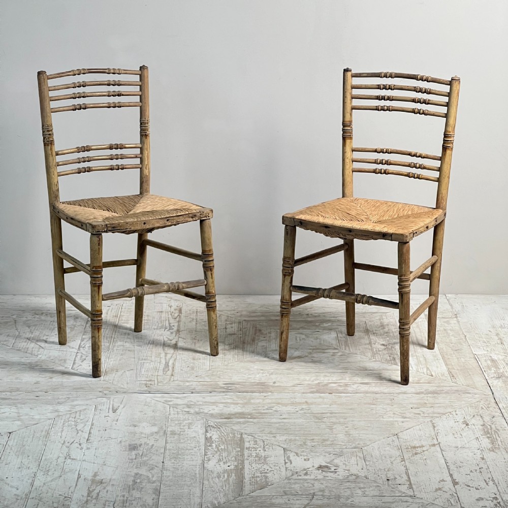 A pair of antique Regency side chairs featuring painted faux bamboo turned frames and woven rush seats.