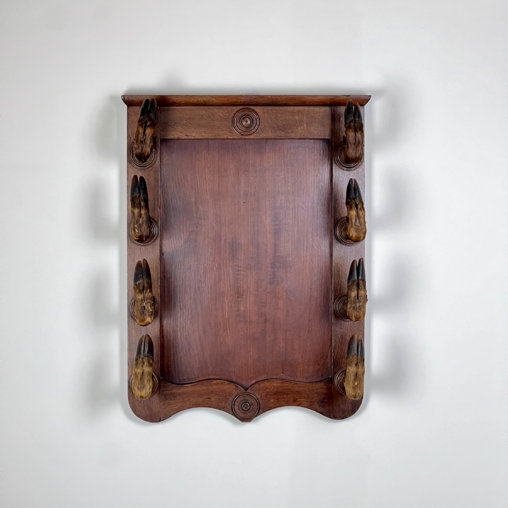 A rectangular dark oak wall rack featuring eight mounted taxidermy deer hooves serving as coat hooks arranged vertically along both sides.