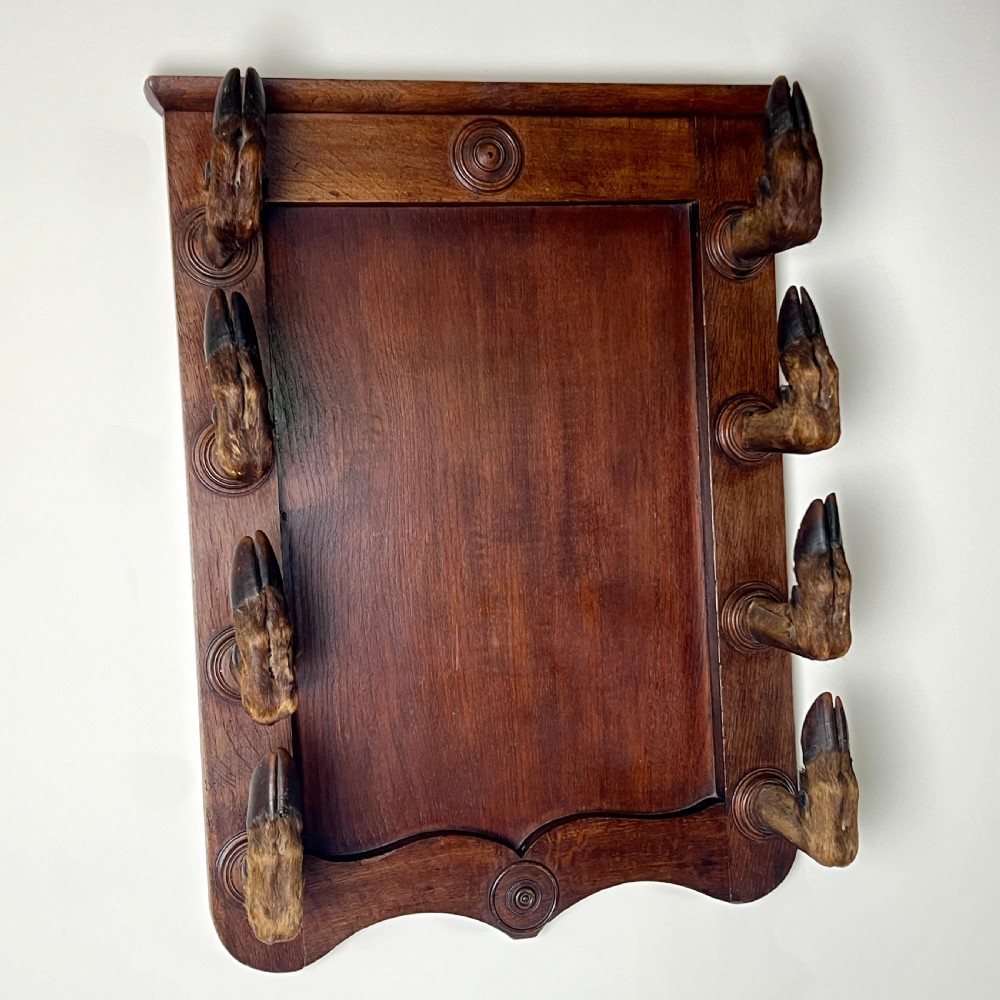 A rectangular dark oak wall rack featuring eight mounted taxidermy deer hooves serving as coat hooks arranged vertically along both sides. View VII