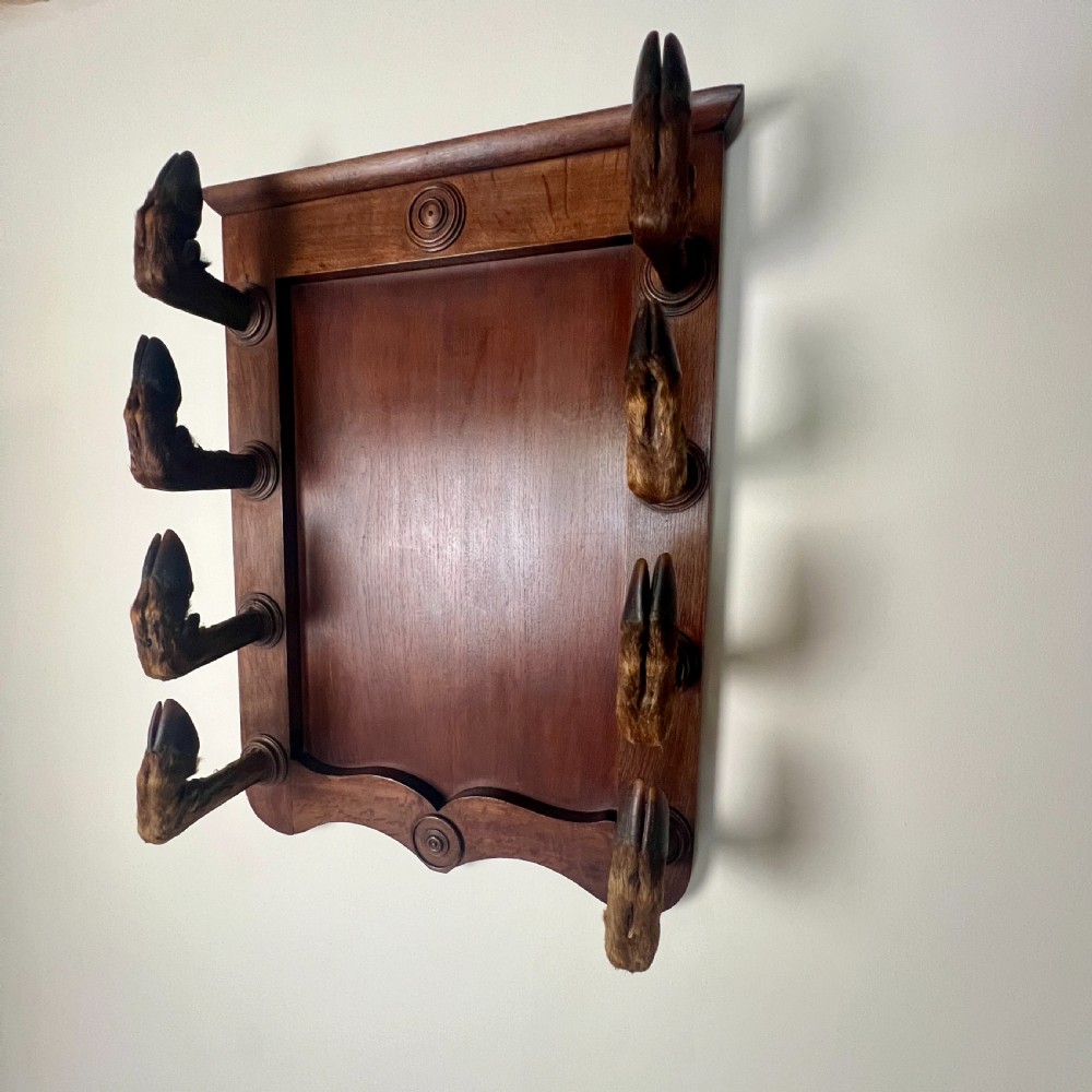 A rectangular dark oak wall rack featuring eight mounted taxidermy deer hooves serving as coat hooks arranged vertically along both sides. View XII