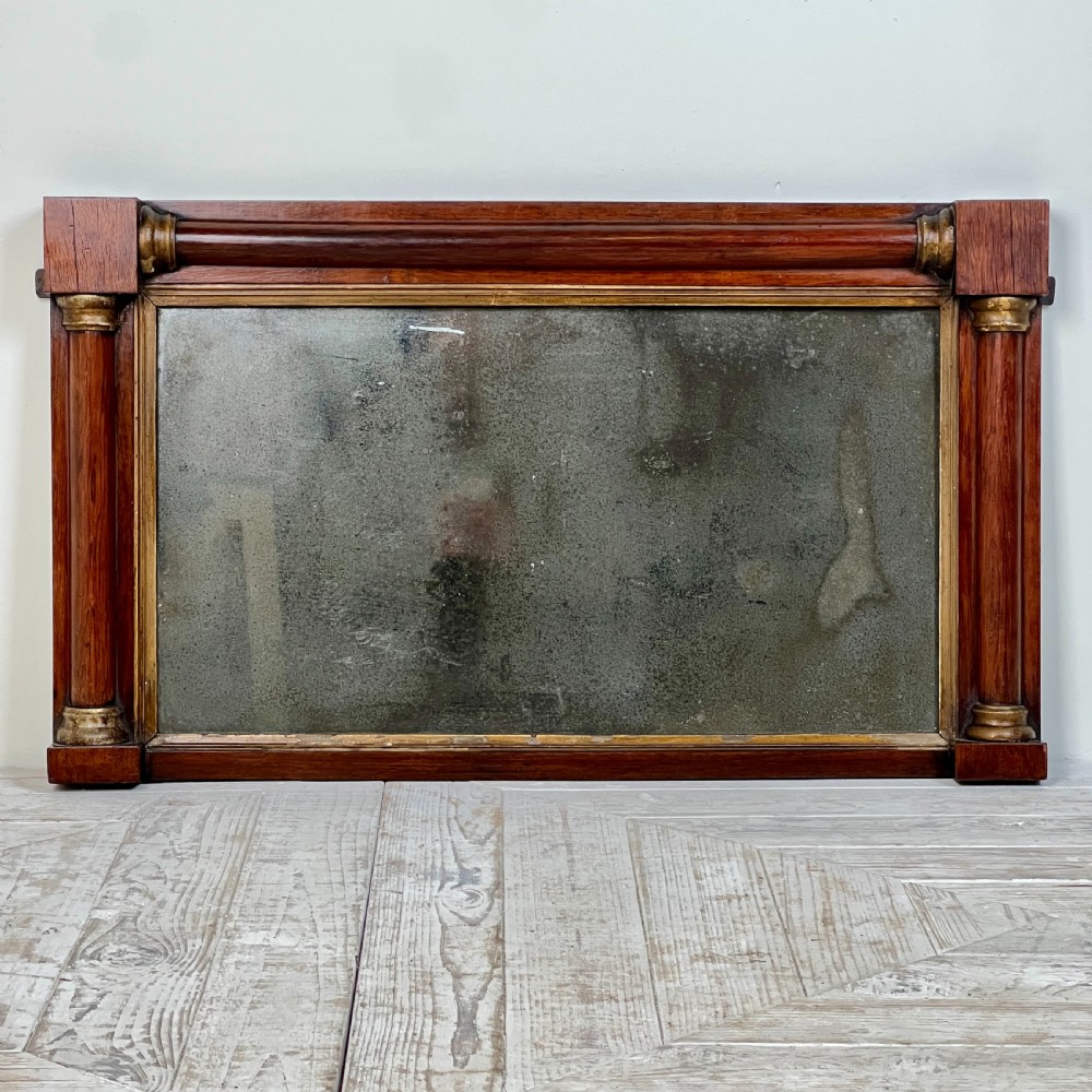 An early 19th-century horizontal mahogany overmantel mirror featuring turned side pilasters, gilt accents, and foxed glass.