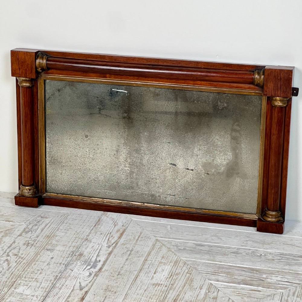 An early 19th-century horizontal mahogany overmantel mirror featuring turned side pilasters, gilt accents, and foxed glass. View II