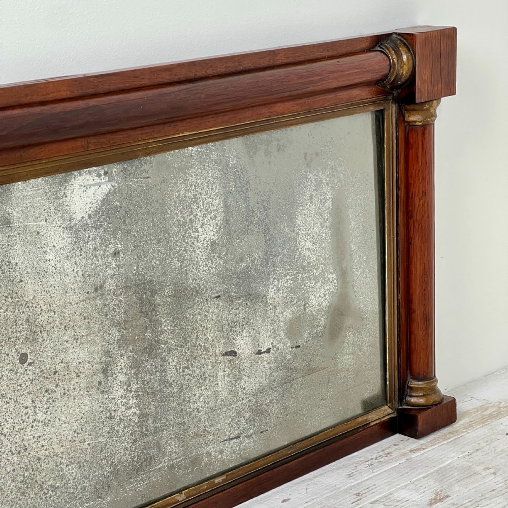 An early 19th-century horizontal mahogany overmantel mirror featuring turned side pilasters, gilt accents, and foxed glass. View IV