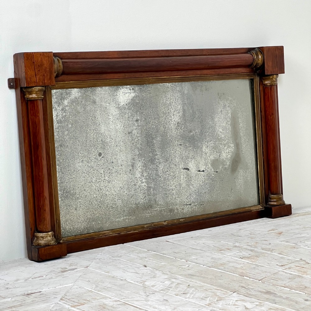 An early 19th-century horizontal mahogany overmantel mirror featuring turned side pilasters, gilt accents, and foxed glass. View V