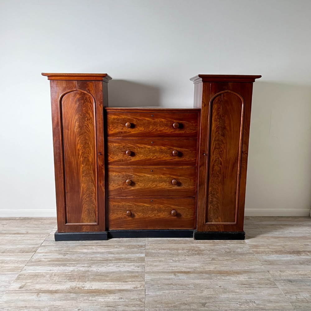 A Victorian flame mahogany breakfront wardrobe featuring a central four-drawer chest flanked by two tall arched cupboards on a plinth base.