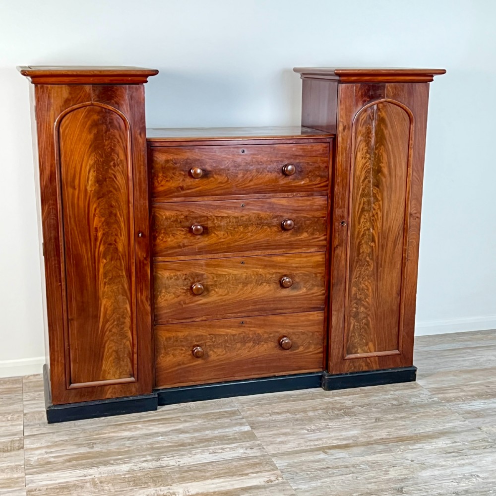 A Victorian flame mahogany breakfront wardrobe featuring a central four-drawer chest flanked by two tall arched cupboards on a plinth base. View II