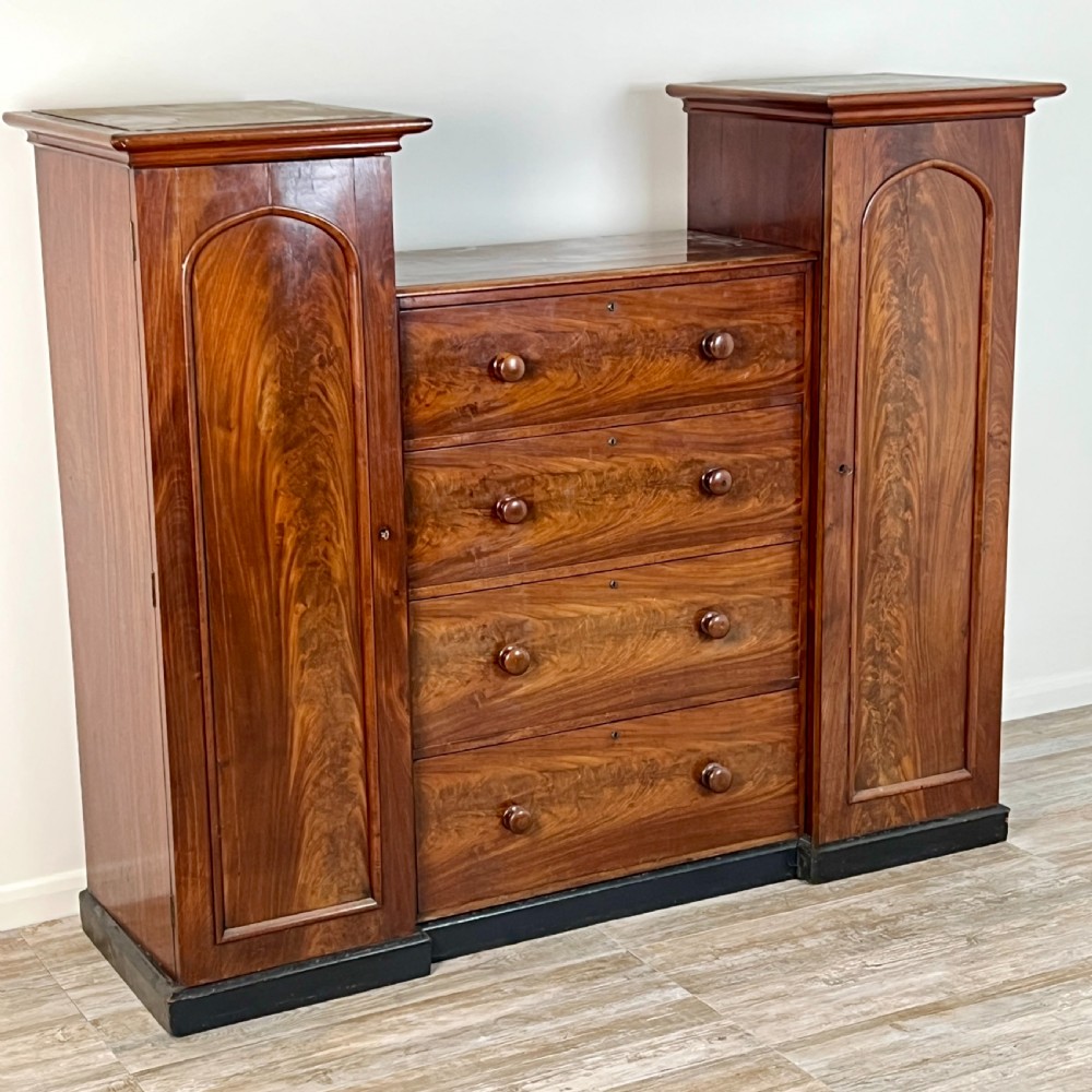 A Victorian flame mahogany breakfront wardrobe featuring a central four-drawer chest flanked by two tall arched cupboards on a plinth base. View III