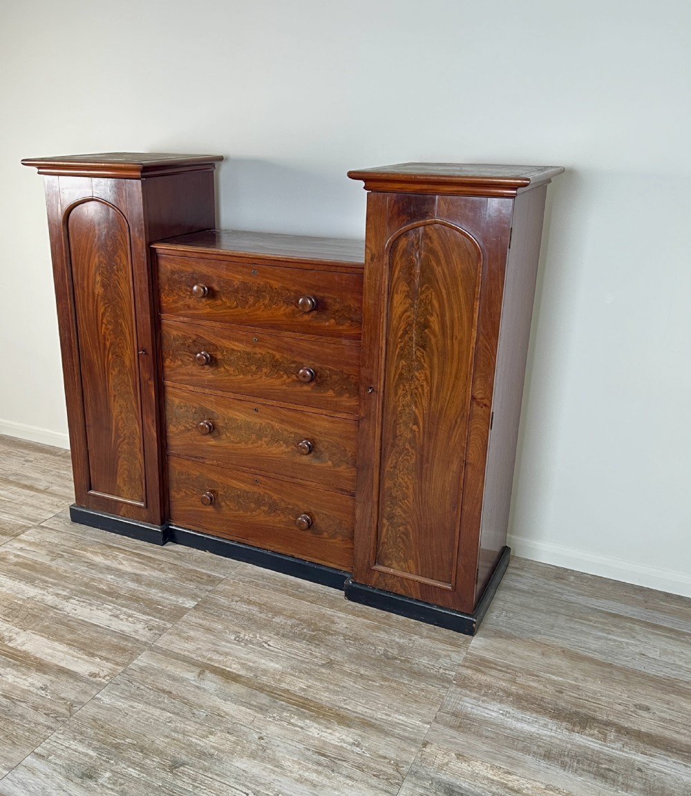 A Victorian flame mahogany breakfront wardrobe featuring a central four-drawer chest flanked by two tall arched cupboards on a plinth base. View VIII