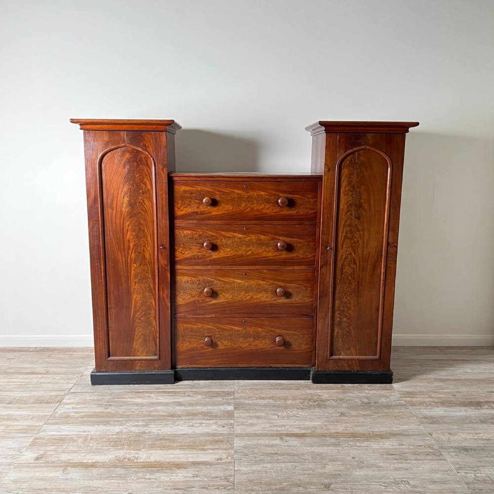 A Victorian flame mahogany breakfront wardrobe featuring a central four-drawer chest flanked by two tall arched cupboards on a plinth base. View IX