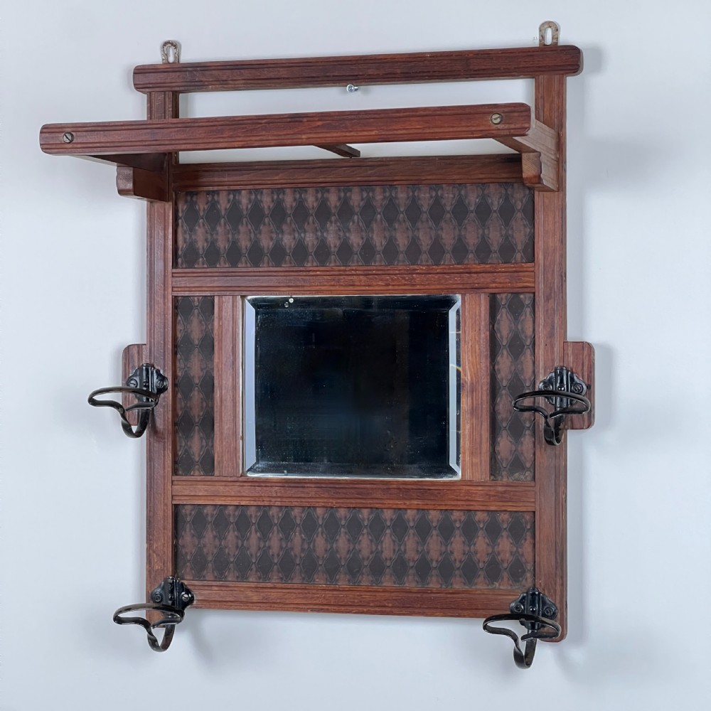 A wall-mounted dark wood coat rack featuring a central bevelled square mirror, geometric diamond pattern panels, an upper hat shelf, and four metal hooks.