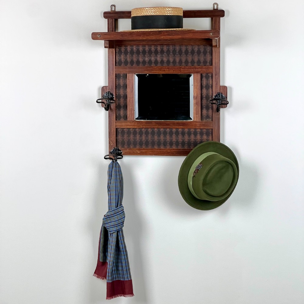 A wall-mounted dark wood coat rack featuring a central bevelled square mirror, geometric diamond pattern panels, an upper hat shelf, and four metal hooks. View II
