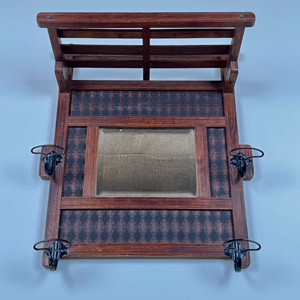 A wall-mounted dark wood coat rack featuring a central bevelled square mirror, geometric diamond pattern panels, an upper hat shelf, and four metal hooks. View IV