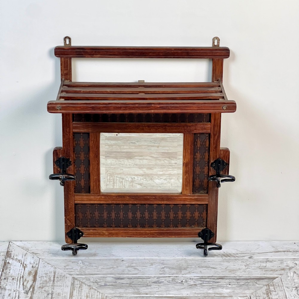 A wall-mounted dark wood coat rack featuring a central bevelled square mirror, geometric diamond pattern panels, an upper hat shelf, and four metal hooks. View VI