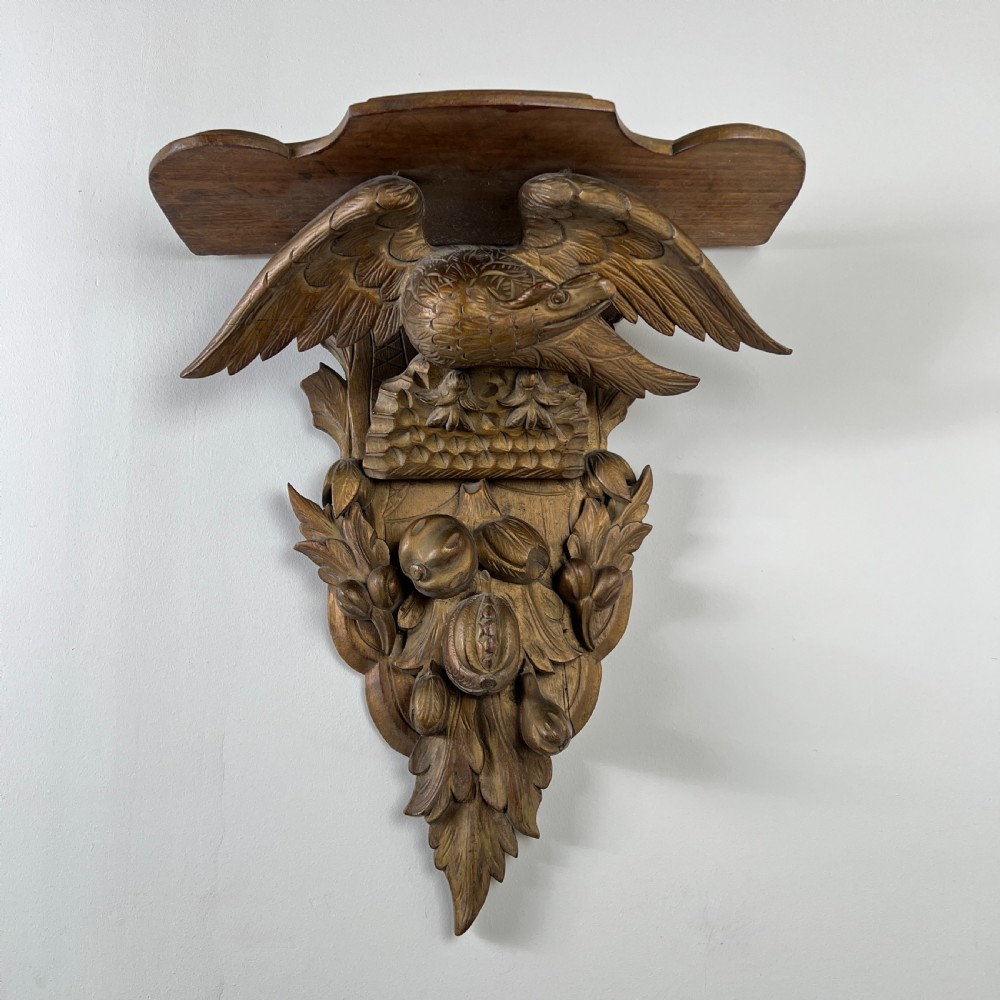 A 19th-century carved giltwood wall bracket featuring a spread-winged eagle above carved fruit and acanthus leaf details.