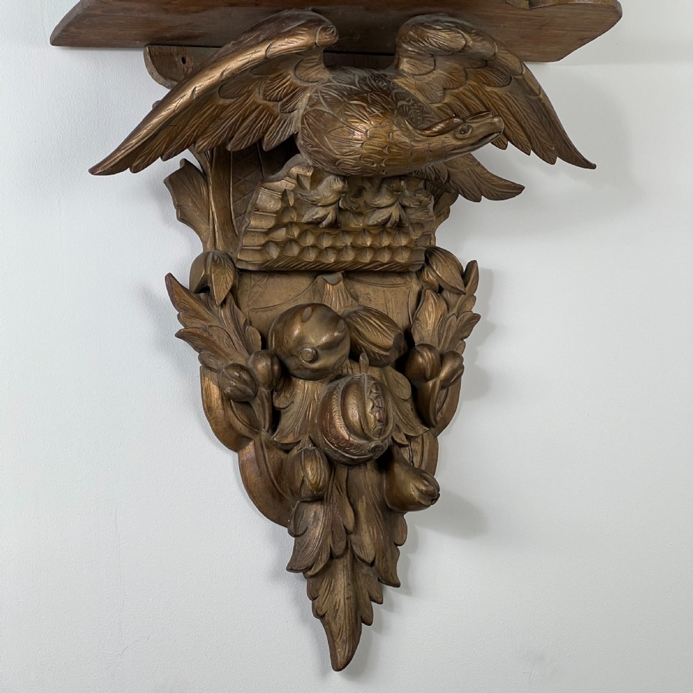 A 19th-century carved giltwood wall bracket featuring a spread-winged eagle above carved fruit and acanthus leaf details. View X